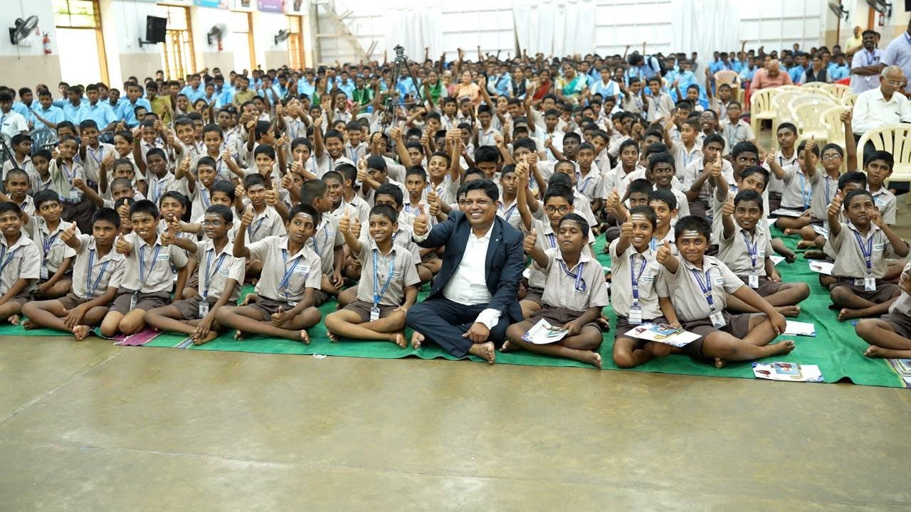 Sarathbabu Elumalai seated among hundreds of school students giving a thumbs up
